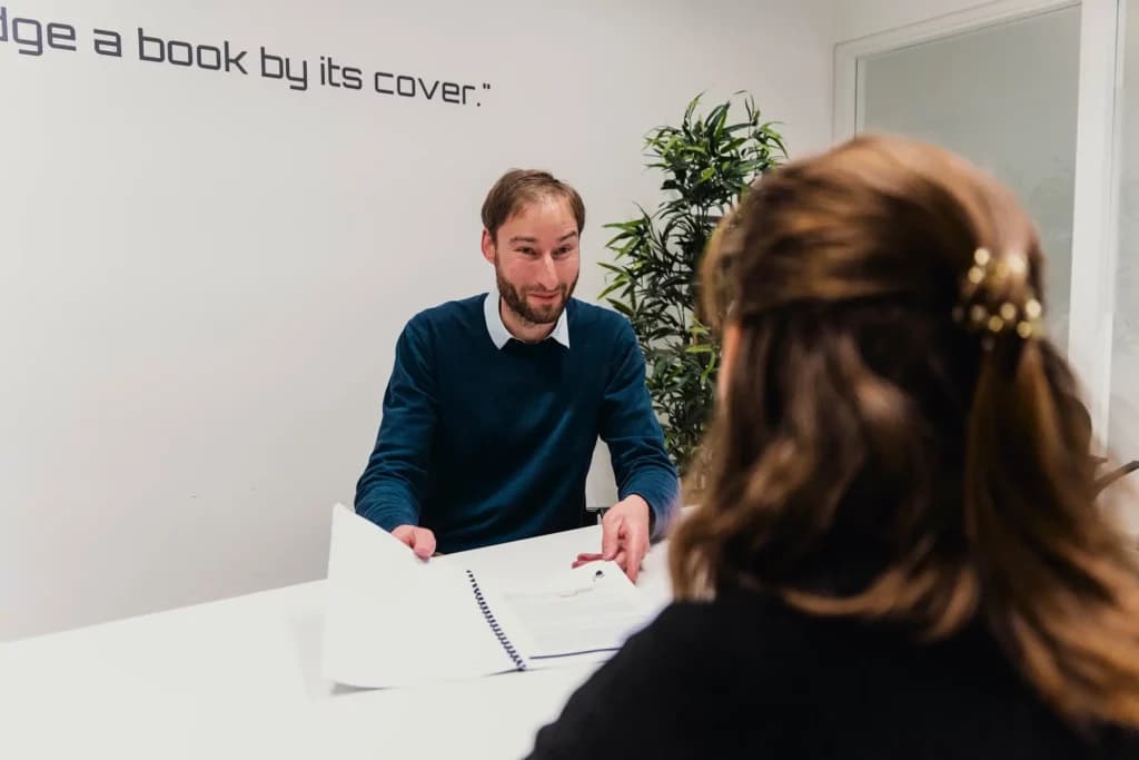 Iemand zit met een klant aan de tafel en geeft uitleg aan de persoon tegenover haar
